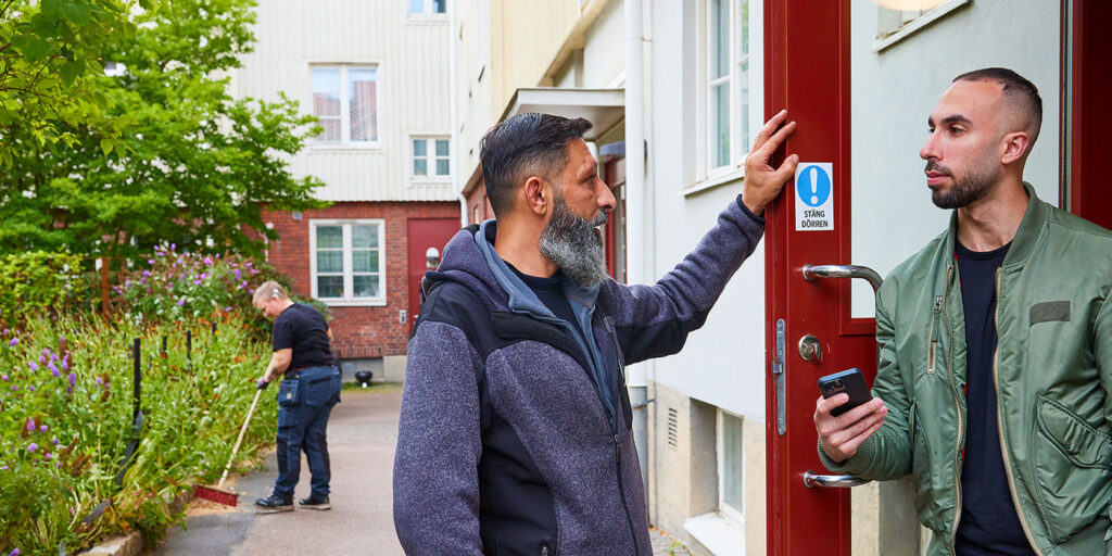 Husvärd i samtal med hyresgäst vid en entrédörr.