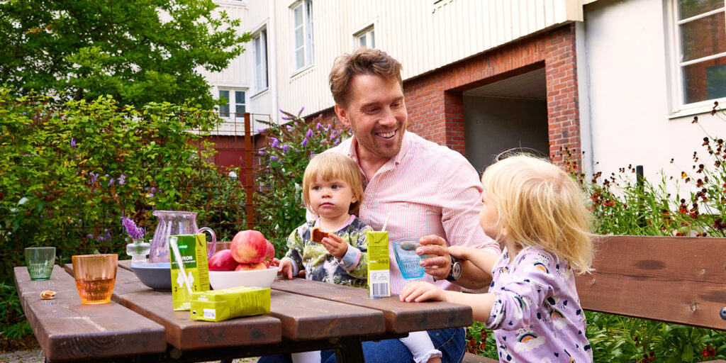 Pappa med två barn fikar på en innergård.