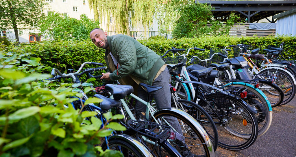 En person låser sin cykel på en grönskande innergård.