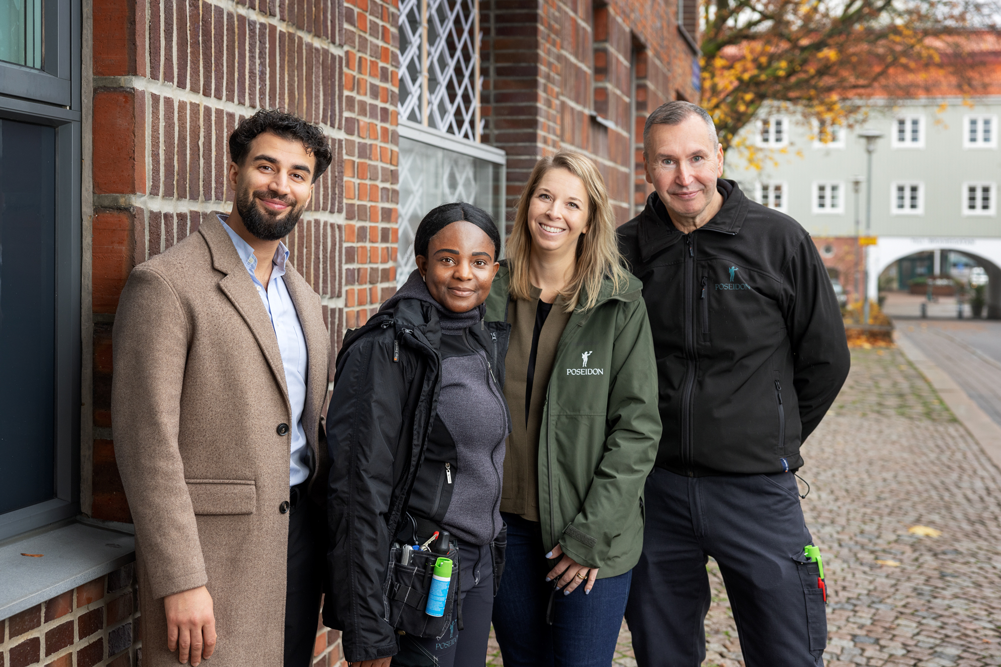 Fyra glada kollegor, en i ullkappa, en i arbetskläder, en i Poseidons gröna tjänstemannajacka, en i arbetskläder. Bakgrund ett fint tegelhus och längre bort ett landshövdingehus.