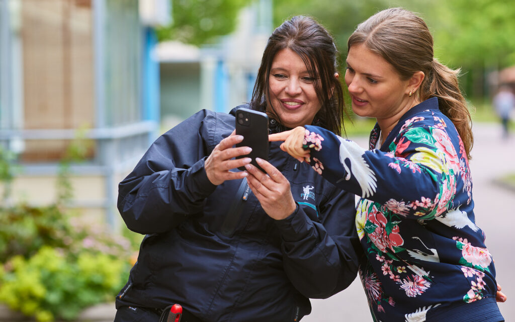 Husvärd visar ung kvinnlig hyresgäst något på sin telefon.