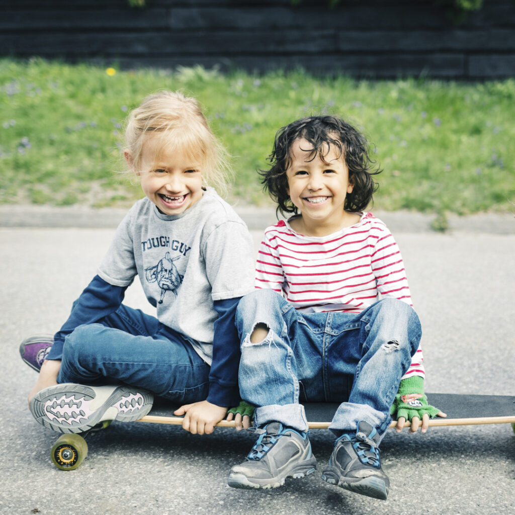 Tre barn leker och skrattar på en skateboard.