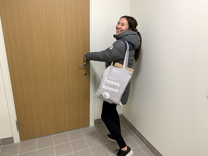 Trapphus: glad tjej med kasse på armen öppnar dörren till en lägenhet