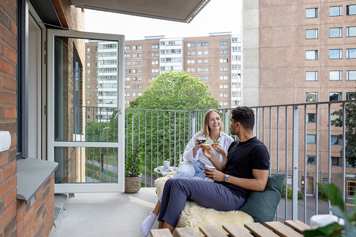 En tjej och en kille på en nyproducerad balkong, sittandes med flerbostadshus bakom. Mandolingatan vid Frölunda Torg.